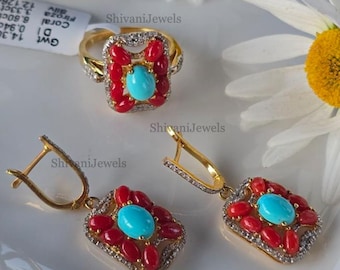 May include: A gold ring and matching earrings set. The ring and earrings feature a central turquoise stone surrounded by red coral and small diamonds. The jewelry is set against a white background with a daisy.
