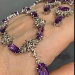 May include: A silver necklace with a purple amethyst pendant and matching earrings. The necklace features a delicate snowflake design with small clear stones.