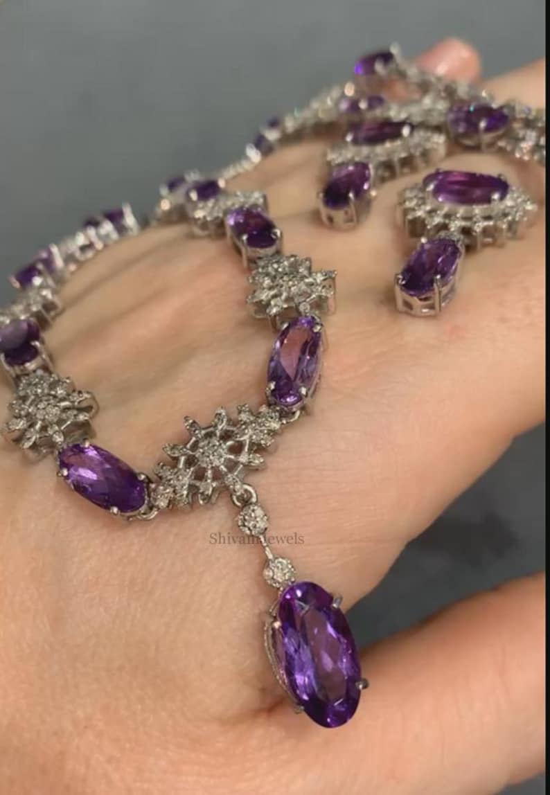May include: A silver necklace with a purple amethyst pendant and matching earrings. The necklace features a delicate snowflake design with small clear stones.