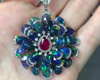 May include: A silver pendant necklace with a flower-shaped design featuring a red gemstone in the centre surrounded by black opals and diamonds.