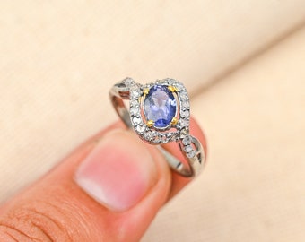 May include: A silver ring with a blue oval gemstone surrounded by smaller white gemstones. The ring has a twisted band.
