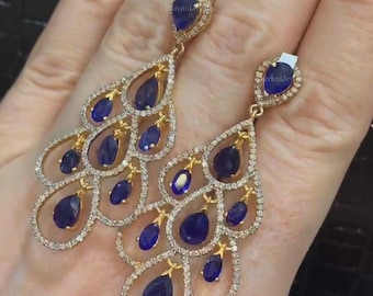 May include: A pair of gold dangle earrings with a teardrop design. The earrings are adorned with blue sapphires and smaller clear diamonds.