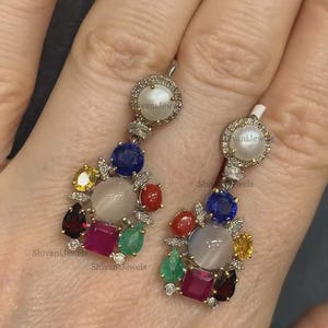 Peut inclure: Paire de boucles d'oreilles pendantes avec un halo de perles et de diamants. Les boucles d'oreilles présentent un groupe de pierres précieuses colorées, dont le bleu, le rouge, le jaune et le vert, dans un arrangement floral. Les boucles d'oreilles sont en métal argenté.