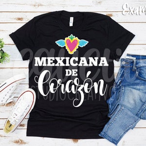May include: Black t-shirt with a white graphic design that says "Mexicana de Coraz&oacute;n" with a pink heart and wings above the text.