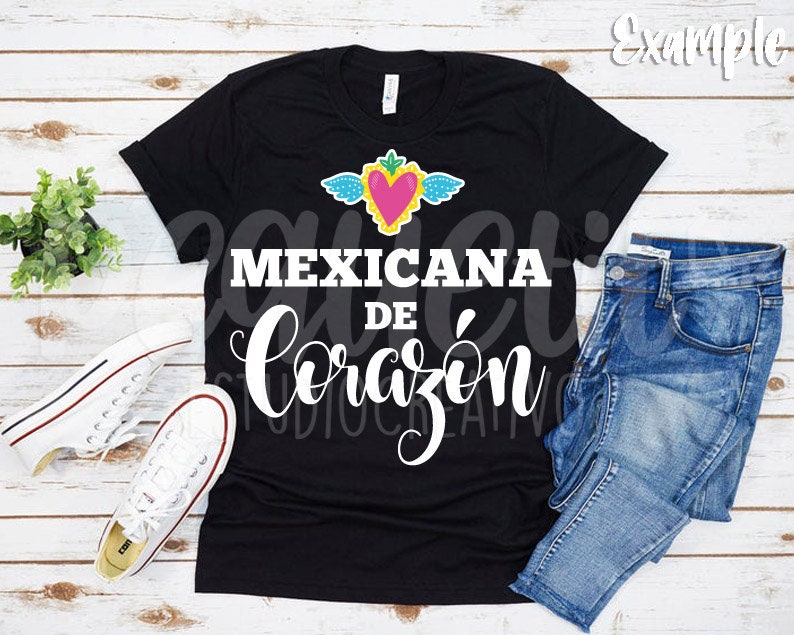 May include: Black t-shirt with a white graphic design that says "Mexicana de Coraz&oacute;n" with a pink heart and wings above the text.