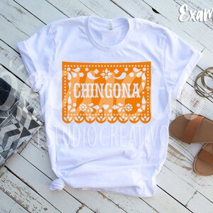 Puede incluir: Camiseta blanca con un dise&ntilde;o de papel recortado naranja que dice "CHINGONA" en texto blanco.