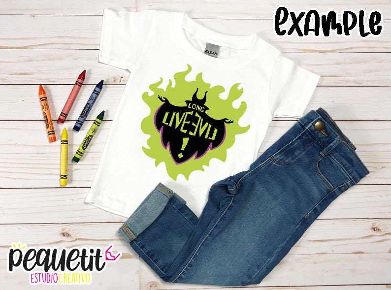 Puede incluir: Camiseta blanca con un gr&aacute;fico verde y negro de un villano de dibujos animados con el texto "Long Live Evil!" impreso en ella. La camiseta est&aacute; colocada sobre una superficie de madera con un par de pantalones vaqueros azules y l&aacute;pices de colores.
