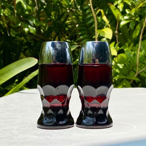 May include: Two dark red glass salt and pepper shakers with silver tops. The shakers have a textured, diamond-shaped pattern.