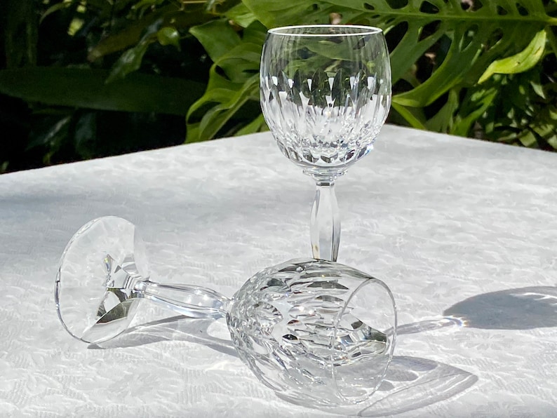 May include: Two clear glass wine glasses with a cut crystal design. The glasses are on a white tablecloth.