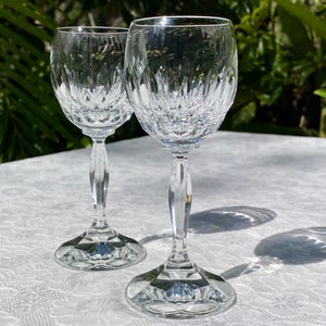 May include: Two clear glass stemmed wine glasses with a cut crystal design. The glasses are on a white tablecloth.