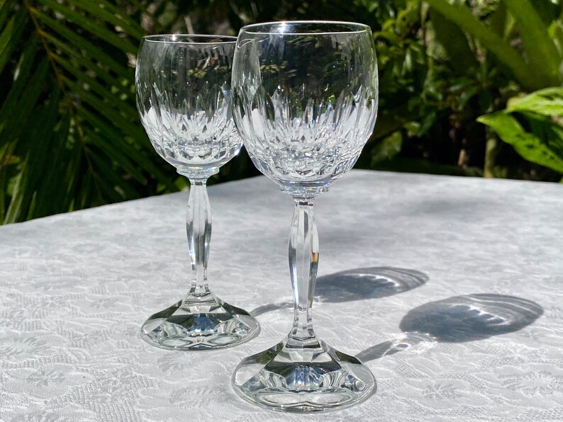 May include: Two clear glass stemmed wine glasses with a cut crystal design. The glasses are on a white tablecloth.