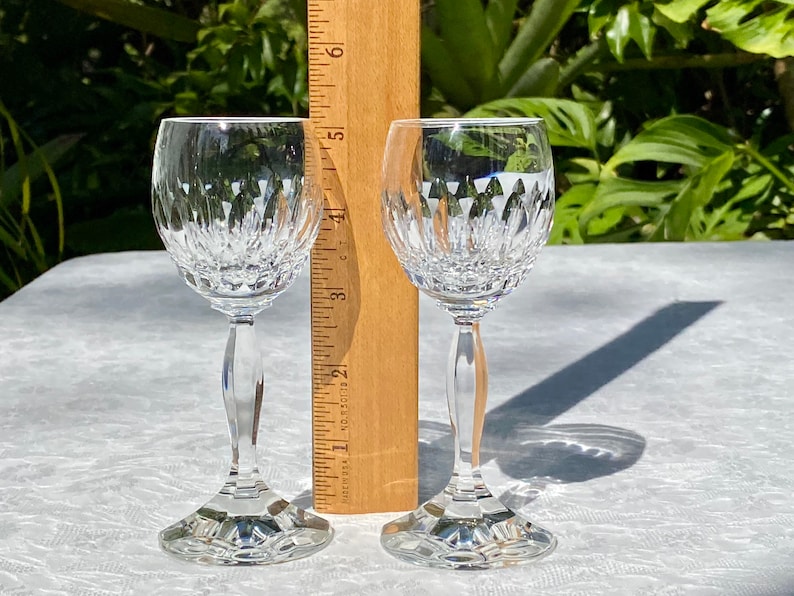 May include: Two clear glass stemmed wine glasses with a cut crystal design. The glasses are on a white tablecloth.