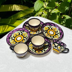May include: Set of four ceramic teacups and saucers with purple, yellow, and black geometric designs.