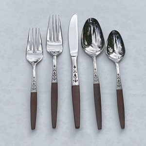 May include: A set of five pieces of silverware: two forks, a knife, and two spoons. The silverware has a shiny, reflective surface with dark brown handles. The handles have a decorative pattern near the top.