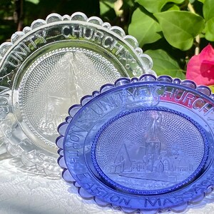 May include: Two vintage glass plates with a scalloped edge. The top plate is clear glass with the words "Unity Church North Easton Mass" etched into the rim. The bottom plate is blue glass with the same words etched into the rim. Both plates feature a church building in the center.