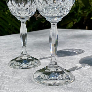 May include: Two clear glass wine glasses with a cut crystal design. The glasses are on a white tablecloth.