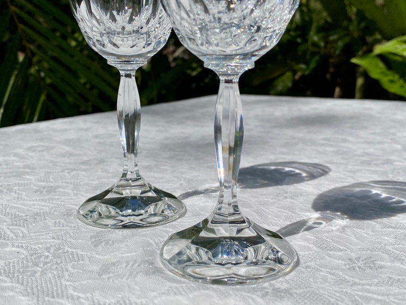 May include: Two clear glass wine glasses with a cut crystal design. The glasses are on a white tablecloth.