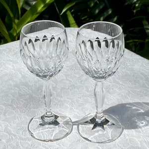 May include: Two clear glass wine glasses with a cut crystal design. The glasses are on a white tablecloth.