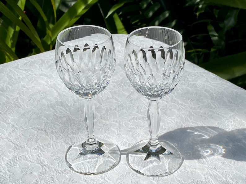 May include: Two clear glass wine glasses with a cut crystal design. The glasses are on a white tablecloth.
