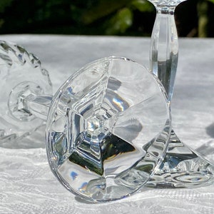 May include: Two clear glass wine glasses with a diamond pattern on the bowl and a faceted stem. The glasses are lying on a white tablecloth.
