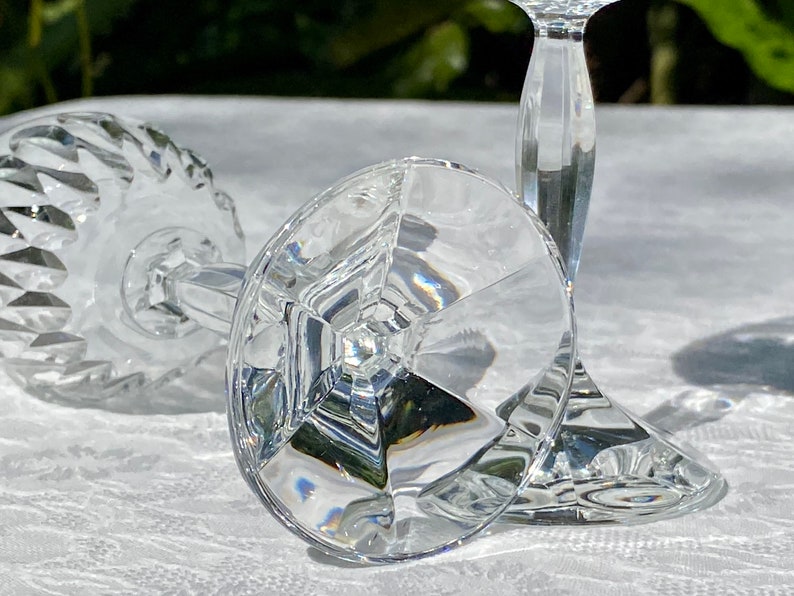 May include: Two clear glass wine glasses with a diamond pattern on the bowl and a faceted stem. The glasses are lying on a white tablecloth.