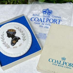 A vintage oval wall plaque that has a silhouette of Queen Elizabeth II.  The cameo style silhouette is black with gold accents and has the dates 1952-1977 underneath her figure.  The back of the plaque reads "Coalport Made in England - Her Majesty Queen Elizabeth II Silver Jubilee 1952-1977 - Silhouette by LJ Arnold."  It has two holes at the top to run a wire for hanging.  Has its original box with original packaging.  Circa 1970s. No damage. Box shows signs of shelf wear. Measures 6" x 4 3/4"