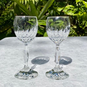 May include: Two clear glass wine glasses with a cut crystal design. The glasses are on a white tablecloth.
