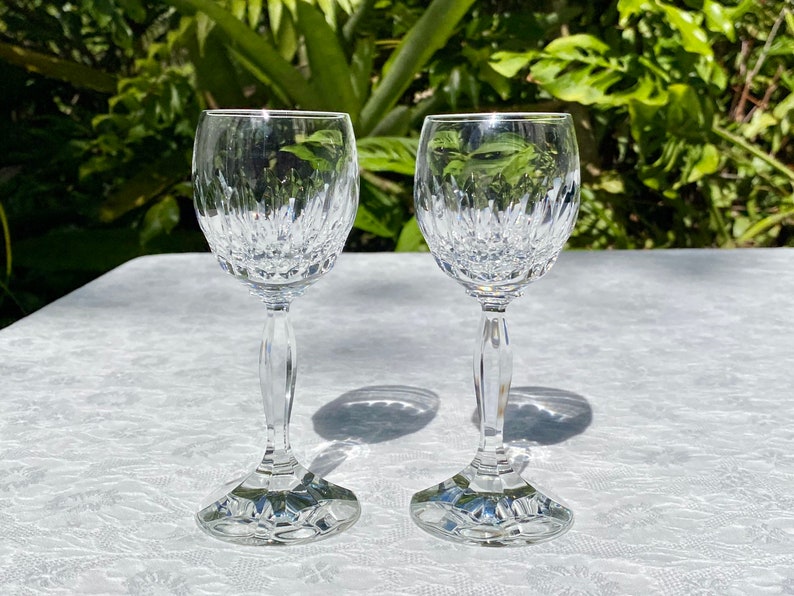 May include: Two clear glass wine glasses with a cut crystal design. The glasses are on a white tablecloth.