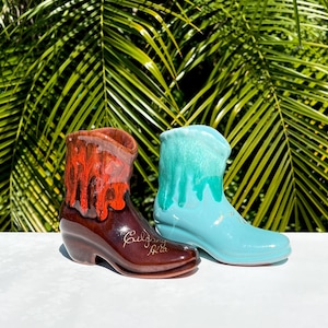 May include: Two ceramic cowboy boot planters, one brown with orange glaze and the other turquoise blue. The brown boot is signed "Belgravia Pottery".