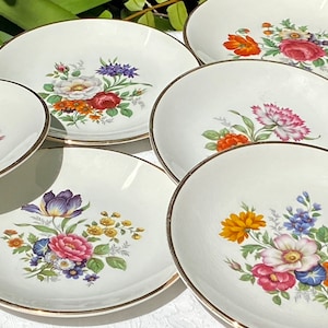 May include: Set of six white ceramic dessert plates with gold trim and floral designs. Each plate features a different colorful floral bouquet with pink, yellow, orange, blue, and purple flowers.