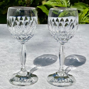 May include: Two clear glass wine glasses with a cut crystal design. The glasses have a tall, slender stem and a round bowl.