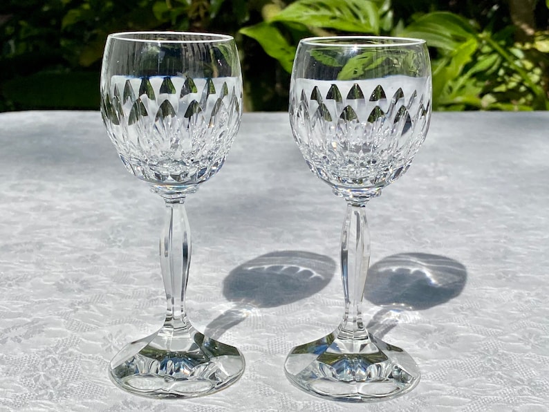 May include: Two clear glass wine glasses with a cut crystal design. The glasses have a tall, slender stem and a round bowl.