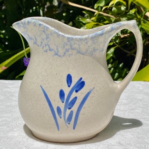 May include: A white ceramic pitcher with a blue and white speckled glaze. The pitcher has a blue floral design and a handle.