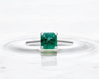 May include: A silver ring with a square emerald green gemstone.