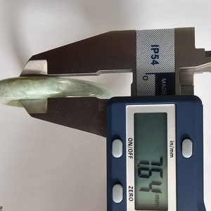 以下が含まれることがあります： デジタルノギスで測定されている翡翠のバングル。ノギスは57.1mmを示しています。