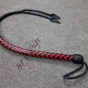 K&ouml;nnte beinhalten: Eine schwarze Lederpeitsche mit einem roten und schwarzen Chevron-Muster. Die Peitsche hat einen geflochtenen Griff und eine lange, spitz zulaufende Peitsche.