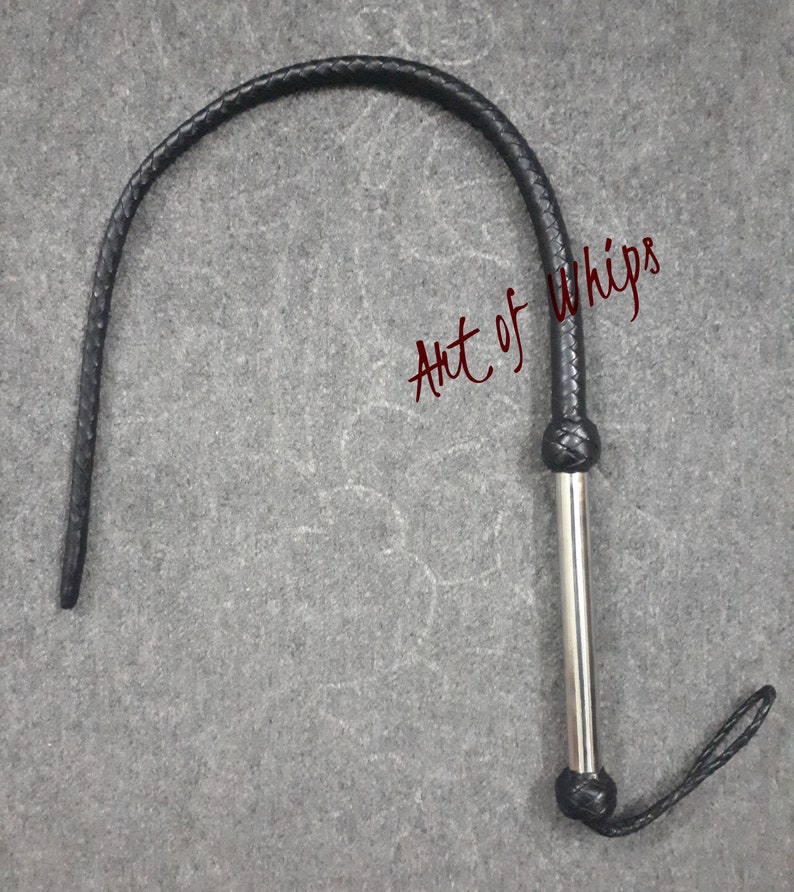 Op de afbeelding: Een zwarte leren zweep met een zilveren handvat en een gevlochten leren lus aan het einde. De zweep is opgerold en het handvat is zichtbaar. De tekst "Art of Whips" is in rood op de achtergrond geschreven.