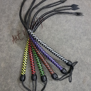 Puede incluir: Seis látigos de cuero con diferentes patrones de chevron de colores. Los látigos son negros con patrones de chevron amarillo, rojo, verde, marrón, morado y plateado.