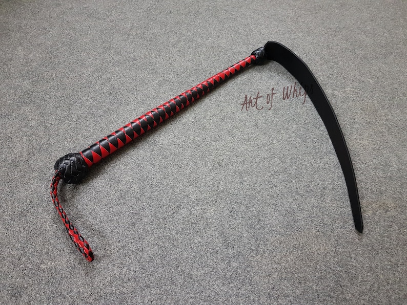 Puede incluir: Un l&aacute;tigo de cuero negro y rojo con un mango trenzado y un l&aacute;tigo largo y curvo. El l&aacute;tigo est&aacute; sobre una alfombra gris. El texto "Art of Whips" es visible en la imagen.