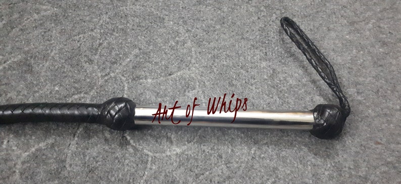 Op de afbeelding: Een zwarte leren zweep met een zilveren metalen kern en een zwarte leren handvat. De zweep is gemarkeerd met "Art of Whips".
