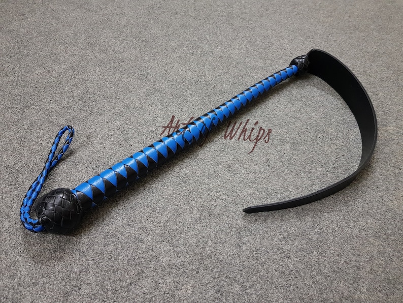Puede incluir: Un l&aacute;tigo de cuero negro con un mango trenzado azul y negro y una larga correa de cuero negro. El l&aacute;tigo mide aproximadamente 76 cm de largo.
