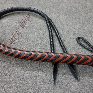 K&ouml;nnte beinhalten: Eine schwarze Lederpeitsche mit einem braunen geflochtenen Lederdesign. Die Peitsche hat einen geflochtenen Griff und einen langen, d&uuml;nnen Schwanz. Der Text "Art of Whips" ist auf der Peitsche sichtbar.
