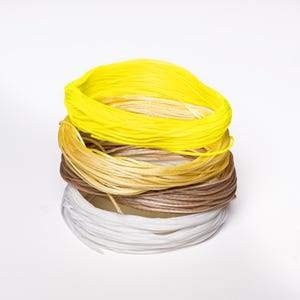 May include: A stack of colourful waxed cord spools in shades of yellow, tan, brown, and white. The spools are neatly coiled, showcasing the different colours and textures of the cord. Ideal for crafting and jewellery making.