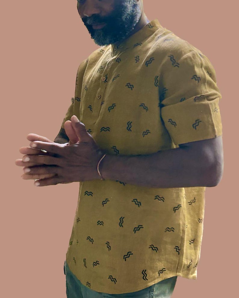 May include: Mustard yellow short-sleeved shirt with a mandarin collar and a pattern of black wave-like shapes. The shirt has a button-down front and rolled-up sleeves. The shirt is made of a lightweight fabric.