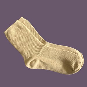 Puede incluir: Un par de calcetines acanalados de color beige claro. Los calcetines est&aacute;n hechos de un material suave y tienen un dise&ntilde;o cl&aacute;sico. Los calcetines se muestran sobre un fondo p&uacute;rpura. Los calcetines son de color neutro.