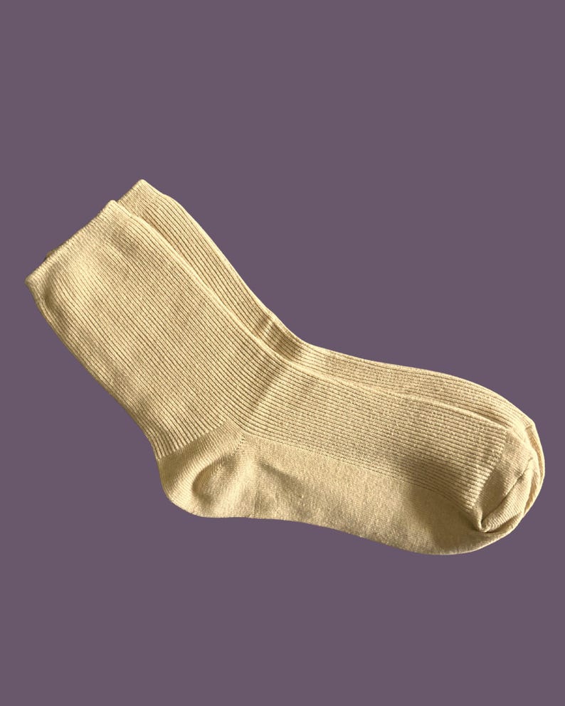 Puede incluir: Un par de calcetines acanalados de color beige claro. Los calcetines est&aacute;n hechos de un material suave y tienen un dise&ntilde;o cl&aacute;sico. Los calcetines se muestran sobre un fondo p&uacute;rpura. Los calcetines son de color neutro.