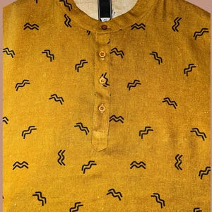 May include: Mustard yellow shirt with a mandarin collar and a button-down placket. The shirt features a repeating pattern of black, wavy lines. The fabric appears to be a textured linen or cotton blend, offering a casual and comfortable look.