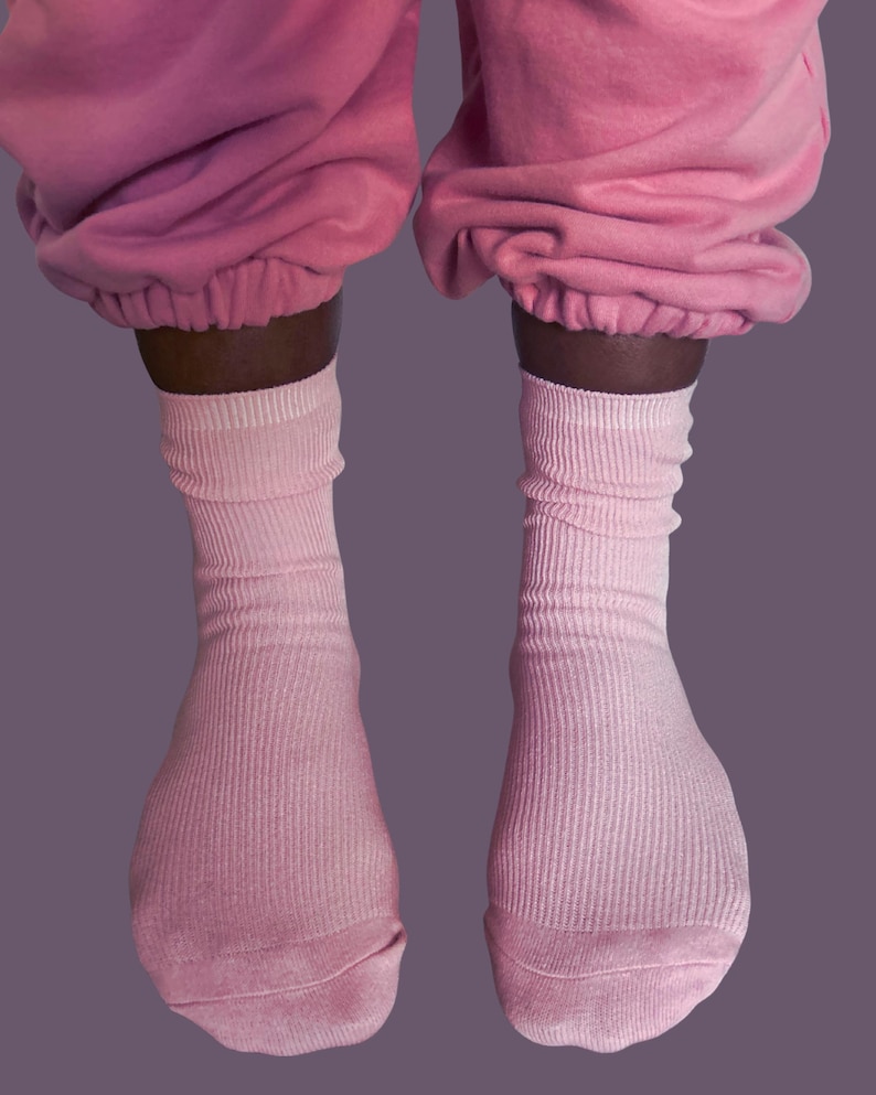 Puede incluir: Se ven dos pares de calcetines de canal&eacute; rosa claro, que se llevan con un pantal&oacute;n de ch&aacute;ndal rosa a juego. Los calcetines est&aacute;n subidos, con la tela recogida alrededor de los tobillos. El fondo es morado.