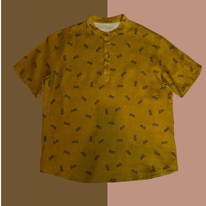 May include: Mustard yellow short-sleeve shirt with a mandarin collar and a three-button placket. The shirt is patterned with small, black, wavy lines. The shirt is made of a lightweight fabric.