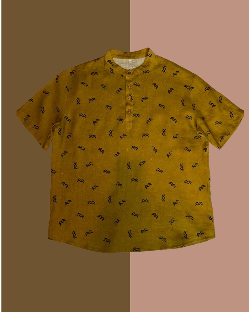 May include: Mustard yellow short-sleeve shirt with a mandarin collar and a three-button placket. The shirt is patterned with small, black, wavy lines. The shirt is made of a lightweight fabric.